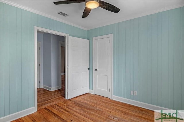 unfurnished bedroom featuring visible vents, baseboards, wooden walls, ornamental molding, and light wood-style flooring