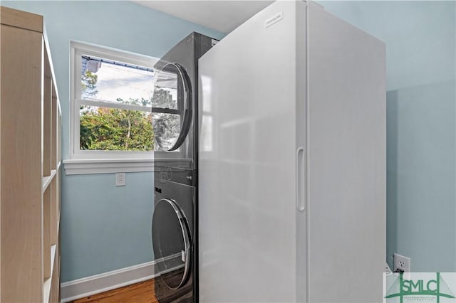 clothes washing area with laundry area, baseboards, stacked washer / drying machine, and wood finished floors