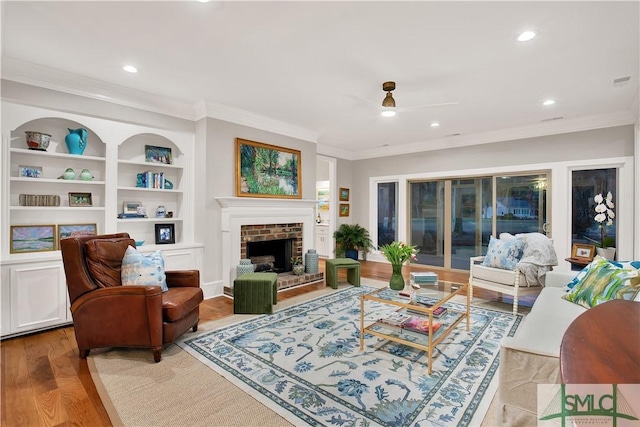 living room with a fireplace, wood finished floors, built in features, and crown molding