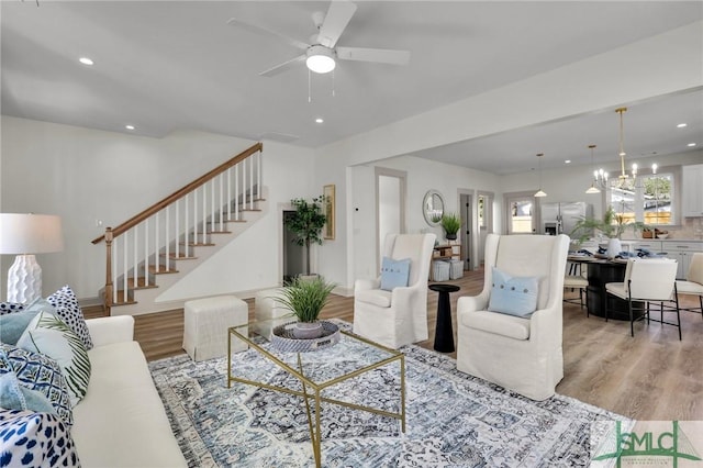 living area with stairs, ceiling fan with notable chandelier, recessed lighting, and light wood-style floors