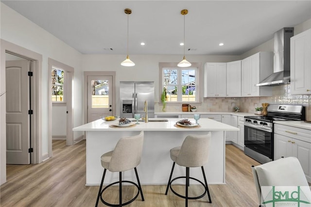 kitchen with a center island with sink, appliances with stainless steel finishes, a sink, wall chimney range hood, and backsplash