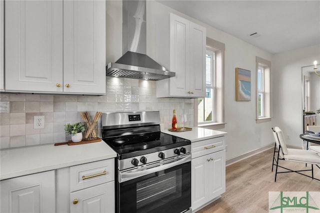 kitchen with wall chimney exhaust hood, light countertops, backsplash, light wood-type flooring, and stainless steel electric range