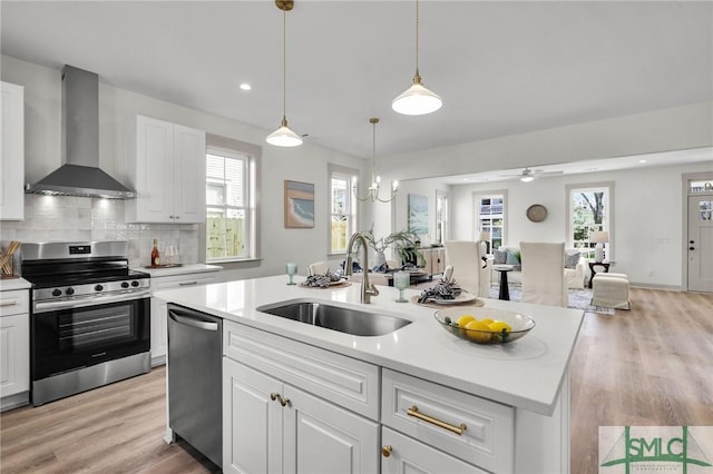 kitchen featuring appliances with stainless steel finishes, open floor plan, light countertops, wall chimney range hood, and a sink