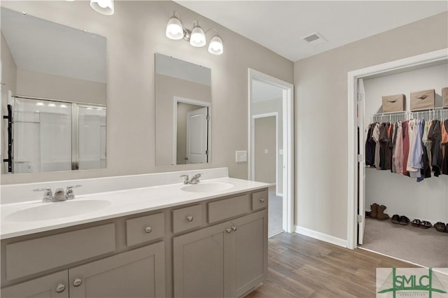 bathroom featuring double vanity, wood finished floors, a sink, and visible vents