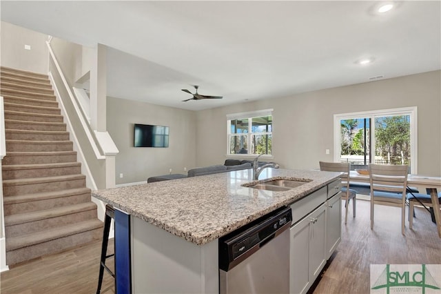 kitchen featuring light stone counters, a healthy amount of sunlight, dishwasher, and a sink