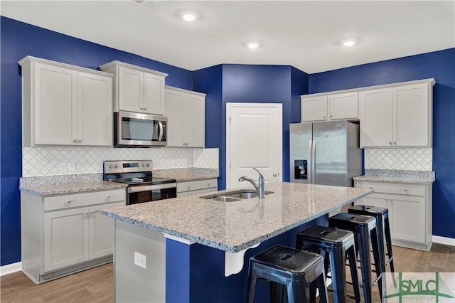 kitchen featuring light wood finished floors, white cabinets, a breakfast bar area, stainless steel appliances, and a sink