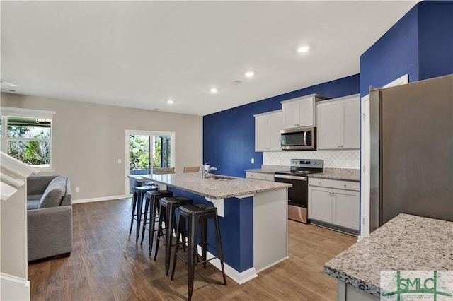 kitchen with a center island with sink, a sink, stainless steel appliances, a kitchen bar, and backsplash