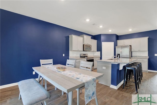 kitchen featuring white cabinets, an island with sink, stainless steel appliances, light wood-style floors, and a sink