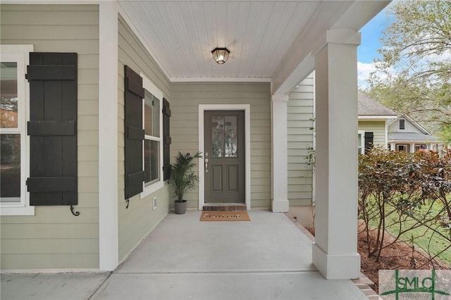 doorway to property featuring covered porch and a shingled roof