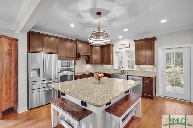 kitchen featuring appliances with stainless steel finishes, light wood-style floors, ornamental molding, a sink, and a kitchen breakfast bar