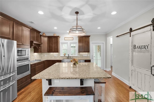 kitchen with a barn door, stainless steel appliances, a kitchen island, a sink, and backsplash