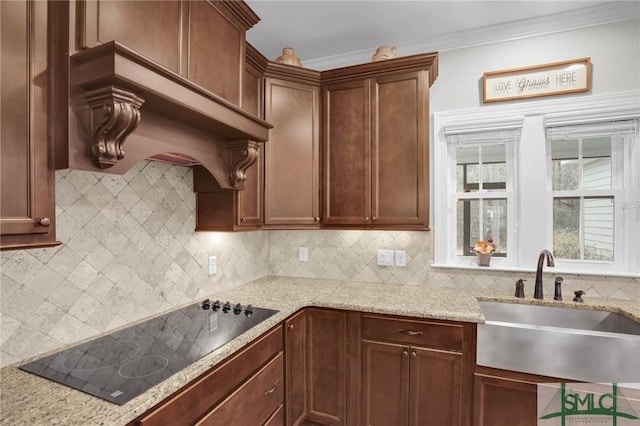 kitchen with black electric stovetop, a sink, light stone countertops, and decorative backsplash