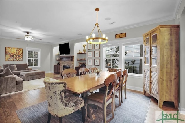 dining space featuring light wood-type flooring, crown molding, and a stone fireplace