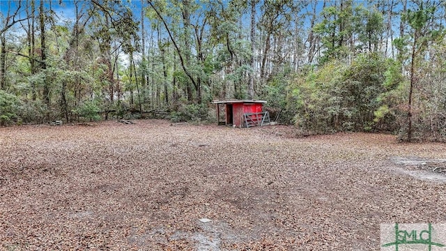 view of yard with an outbuilding, a forest view, and a storage unit