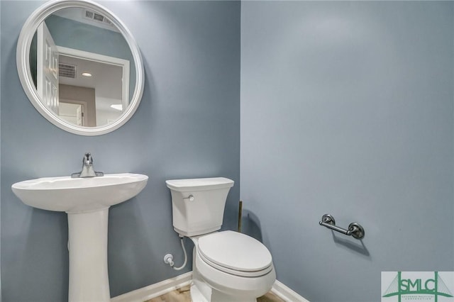 half bath with baseboards, visible vents, toilet, and wood finished floors