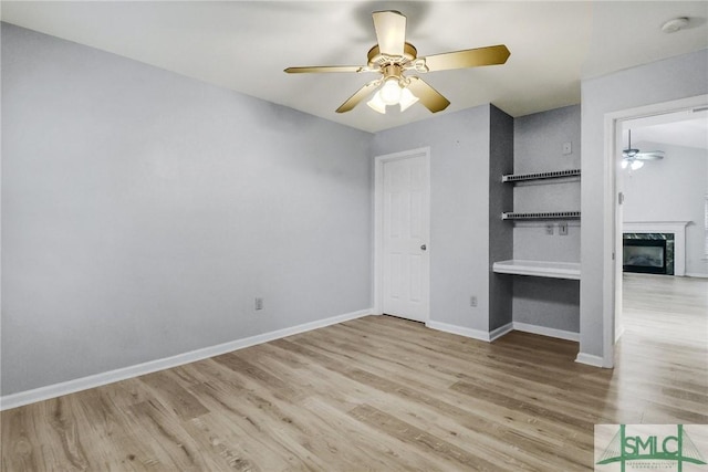 unfurnished bedroom with a ceiling fan, a premium fireplace, baseboards, and wood finished floors