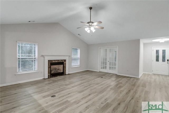 unfurnished living room with light wood-style floors, lofted ceiling, french doors, and a premium fireplace