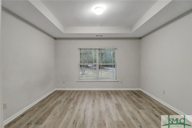 spare room with baseboards, a tray ceiling, and wood finished floors