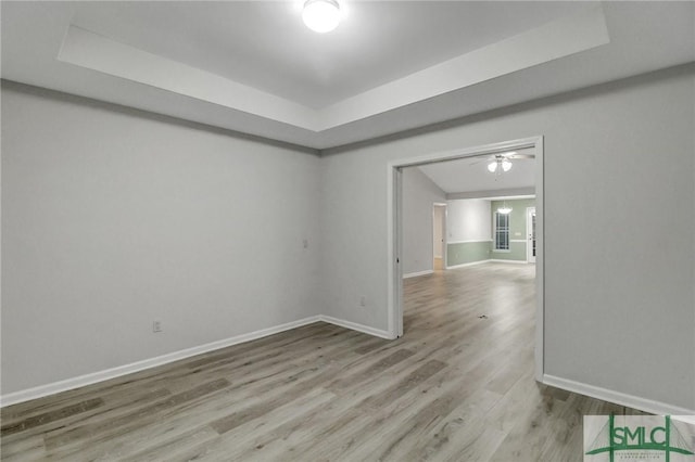 spare room with a raised ceiling, baseboards, and wood finished floors