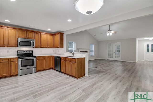 kitchen featuring stainless steel appliances, brown cabinetry, a sink, and a peninsula