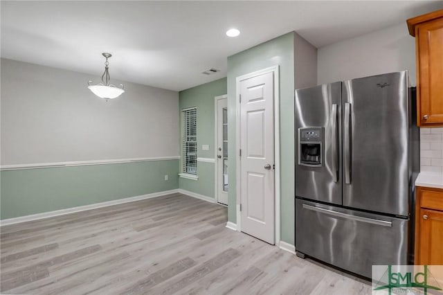 kitchen with light wood finished floors, tasteful backsplash, baseboards, brown cabinets, and stainless steel refrigerator with ice dispenser