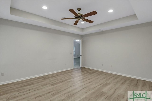 spare room with light wood-style flooring, baseboards, and a raised ceiling