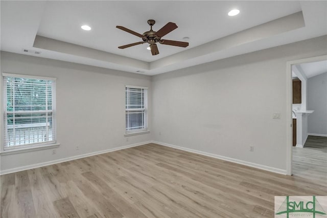 spare room with light wood-style flooring, recessed lighting, a ceiling fan, baseboards, and a tray ceiling