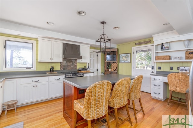 kitchen featuring dark countertops, white cabinets, light wood finished floors, and wall chimney exhaust hood