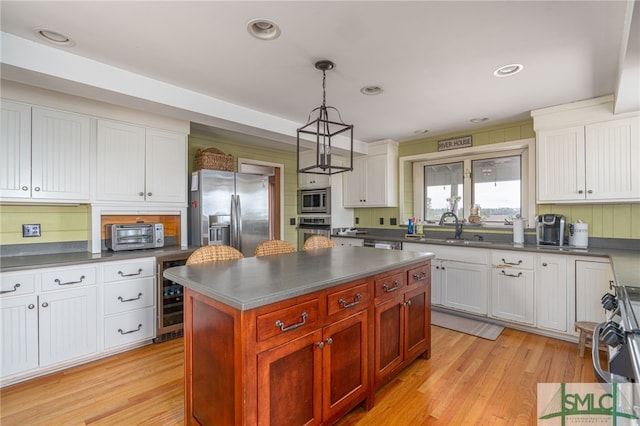 kitchen with dark countertops, light wood-style flooring, appliances with stainless steel finishes, a sink, and beverage cooler