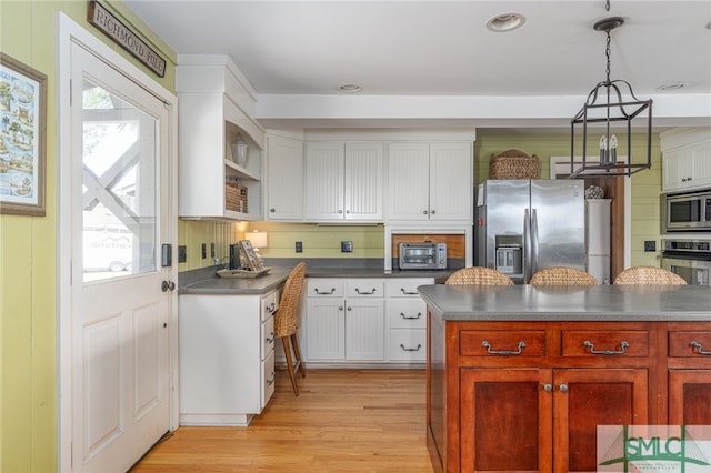 kitchen with a toaster, dark countertops, appliances with stainless steel finishes, light wood-style floors, and white cabinets