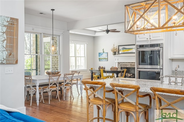 kitchen featuring light stone counters, double oven, a brick fireplace, white cabinetry, and light wood-type flooring