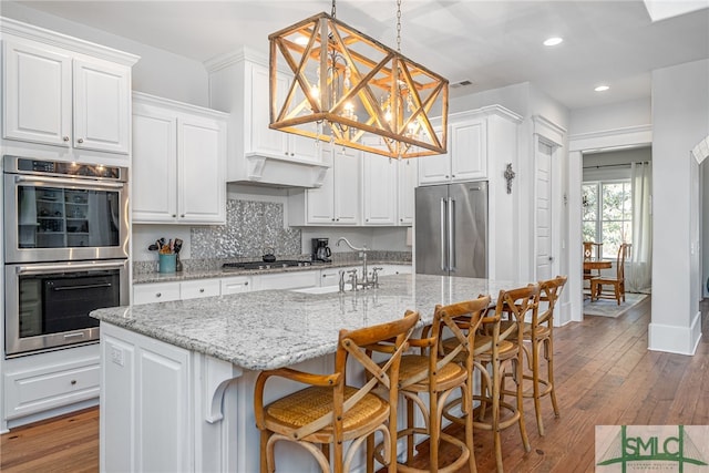 kitchen with appliances with stainless steel finishes, backsplash, hardwood / wood-style flooring, and white cabinets