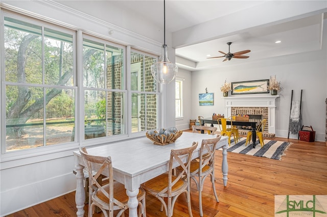 dining area with a tray ceiling, recessed lighting, light wood-style floors, a ceiling fan, and a brick fireplace