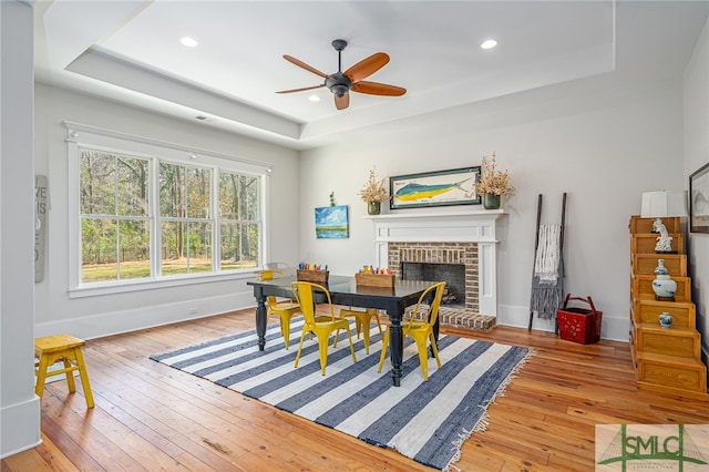 dining space with a fireplace, a raised ceiling, light wood-style flooring, and baseboards