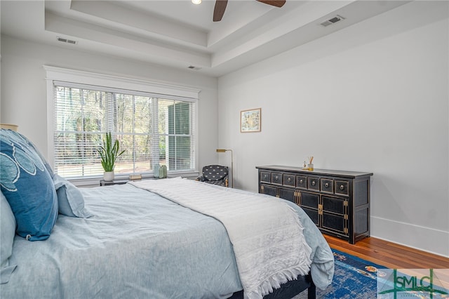 bedroom with baseboards, visible vents, a raised ceiling, and wood finished floors