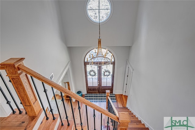 foyer entrance with french doors, stairway, a towering ceiling, wood finished floors, and a chandelier