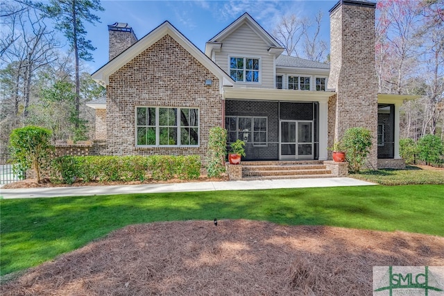 back of property featuring brick siding, a yard, a chimney, entry steps, and a sunroom