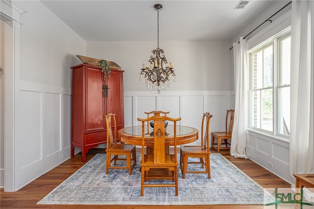 dining area with dark wood-style flooring, an inviting chandelier, visible vents, and a decorative wall