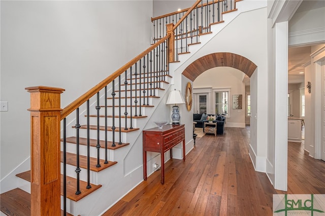 entrance foyer featuring arched walkways, baseboards, a towering ceiling, and hardwood / wood-style floors