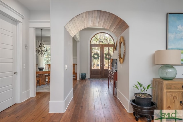 entryway with arched walkways, a chandelier, hardwood / wood-style flooring, and baseboards