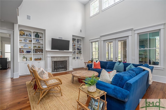 living area featuring built in features, french doors, a fireplace, hardwood / wood-style floors, and baseboards