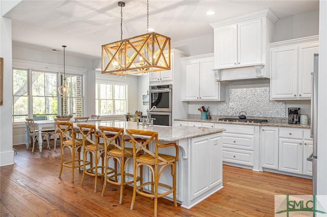 kitchen with stainless steel appliances, white cabinetry, light wood finished floors, an island with sink, and tasteful backsplash