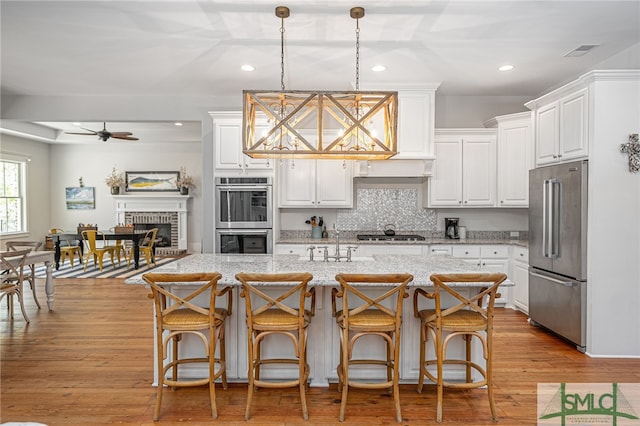 kitchen featuring visible vents, white cabinets, stainless steel appliances, light wood-type flooring, and a brick fireplace