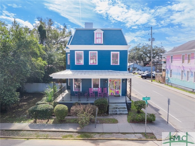 victorian home with mansard roof, a chimney, metal roof, fence, and a porch