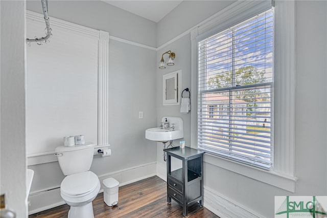 bathroom featuring toilet, a baseboard heating unit, a sink, wood finished floors, and baseboards