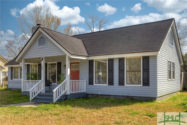 view of front facade with covered porch, roof with shingles, a front lawn, and a chimney