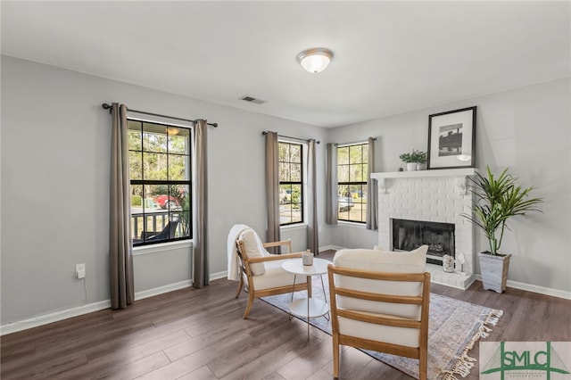 sitting room with a brick fireplace, wood finished floors, visible vents, and baseboards