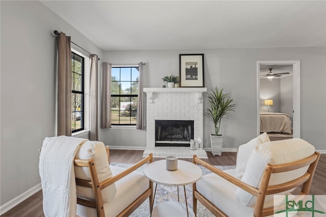 living room featuring a brick fireplace, baseboards, and wood finished floors