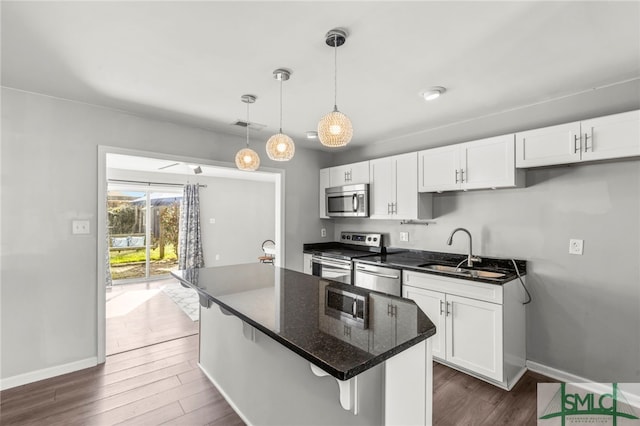 kitchen with dark wood-style flooring, stainless steel appliances, white cabinets, a sink, and a kitchen island