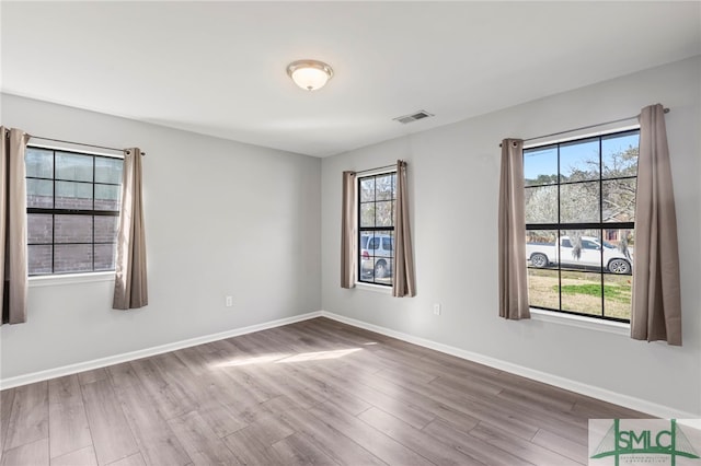 unfurnished room featuring a wealth of natural light, visible vents, baseboards, and wood finished floors